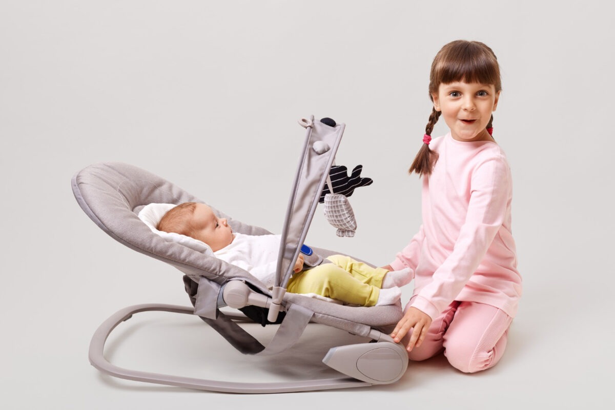 adorable-dark-haired-girl-with-pigtails-plays-with-newborn-sister-brother-who-is-lying-baby-rockers